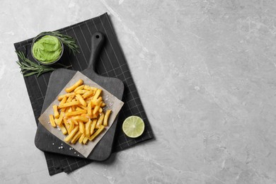 Photo of Serving board with french fries, lime, rosemary and avocado dip on grey table, top view. Space for text