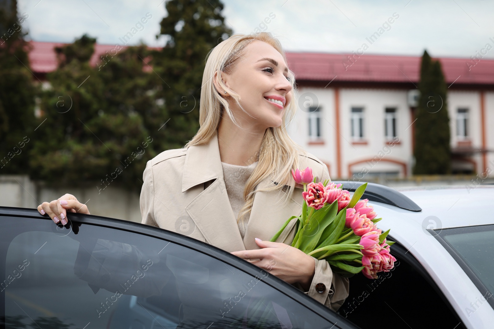 Photo of Happy young woman with beautiful bouquet near car outdoors