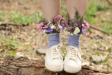 Photo of Woman standing on log with flowers in socks outdoors, closeup