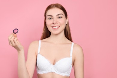 Photo of Woman in bra holding condom on pink background. Safe sex