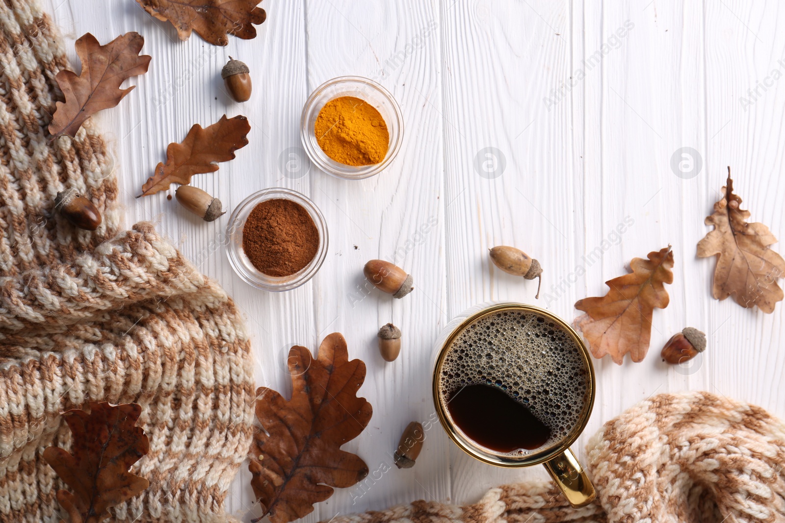 Photo of Cup of hot drink, spices, leaves and knitted scarf on white wooden table, flat lay. Cozy autumn atmosphere