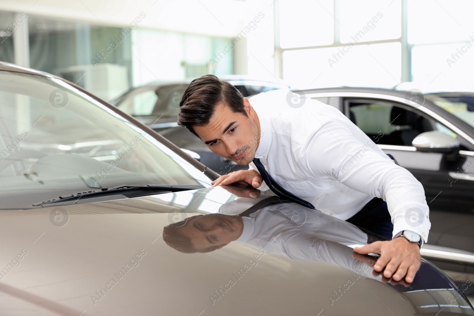 Photo of Young man checking new car in modern dealership