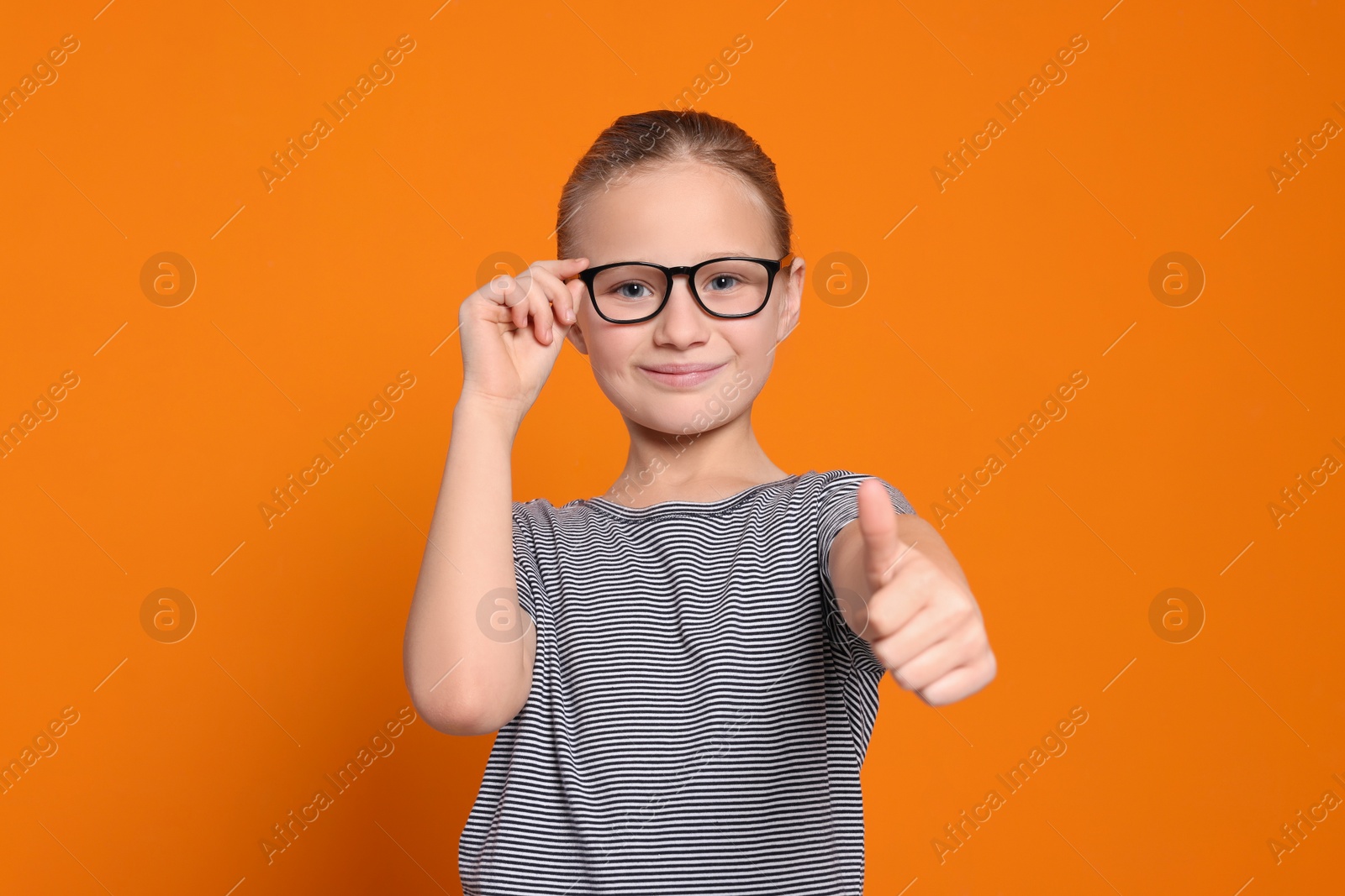 Photo of Cute girl in glasses showing thumb up on orange background