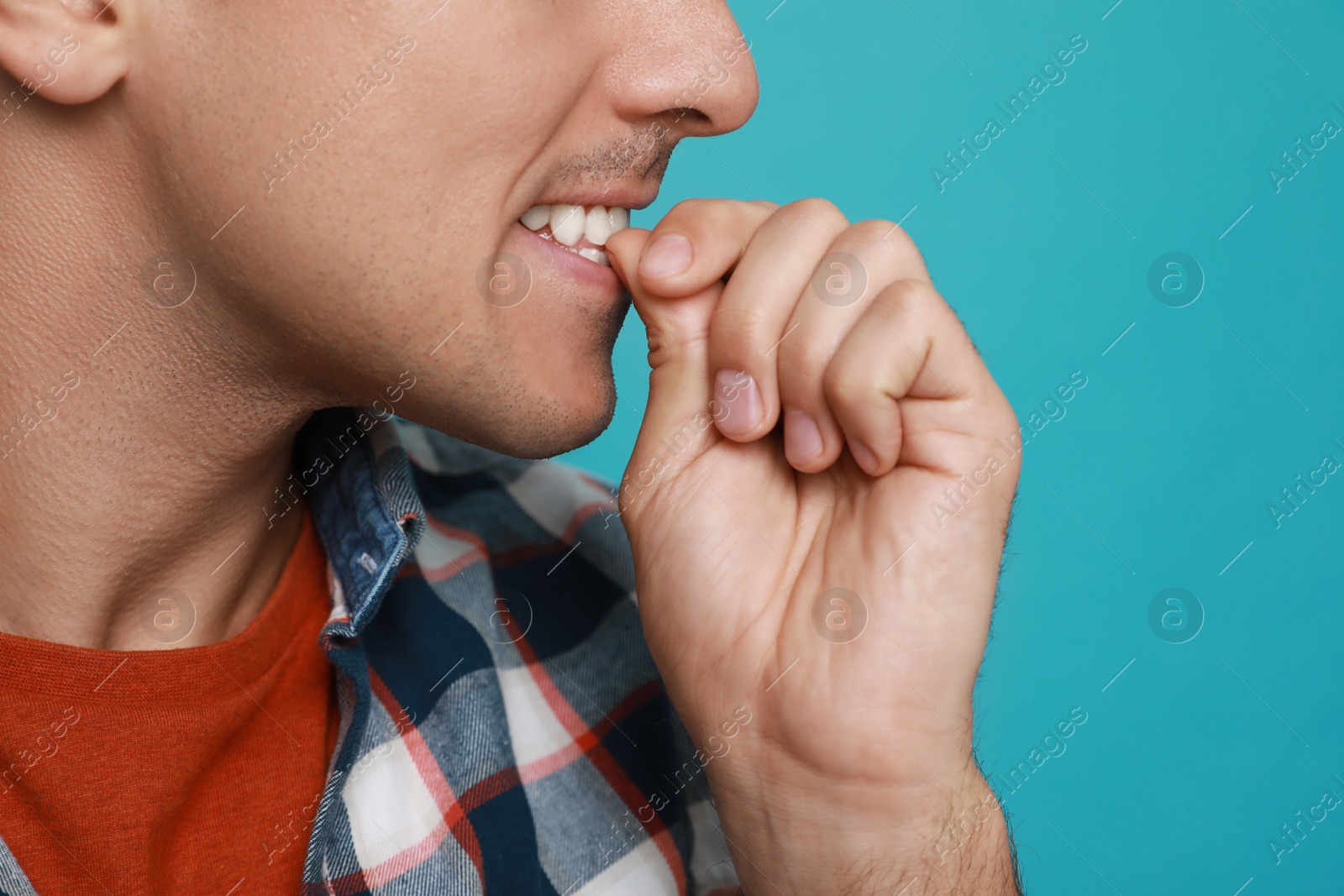 Photo of Man biting his nails on light blue background, closeup. Bad habit