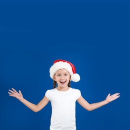 Image of Happy little child in Santa hat on blue background. Christmas celebration