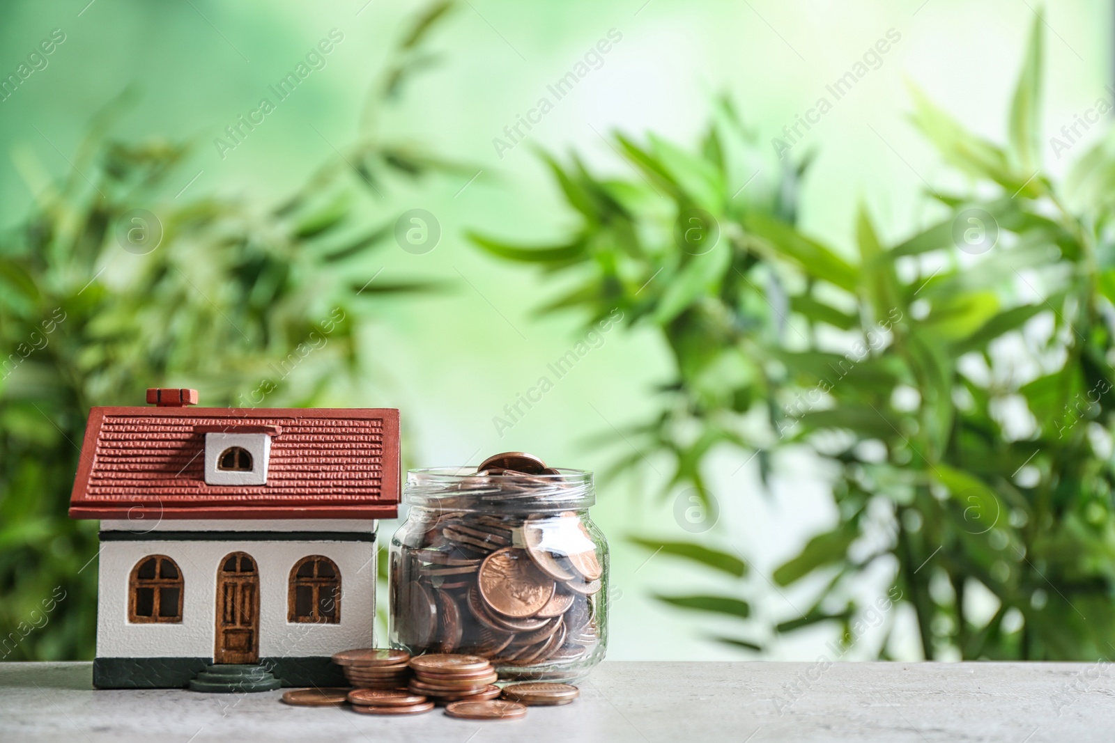 Photo of House model and jar with coins on table against blurred background. Space for text