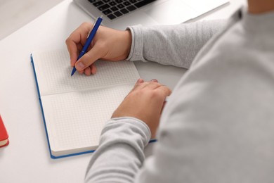 Young man writing in notebook at white table, closeup