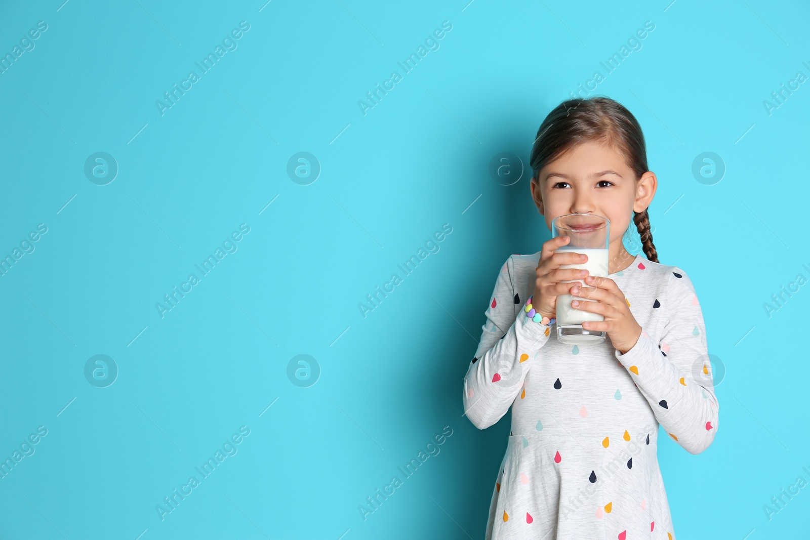 Photo of Cute little girl drinking milk on color background