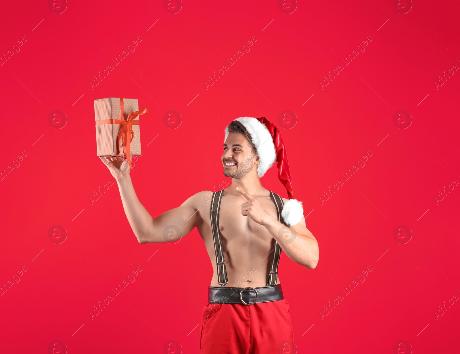 Photo of Shirtless sexy young Santa Claus with gift on color background