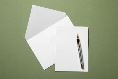 Blank sheet of paper, letter envelope and pen on green background, top view