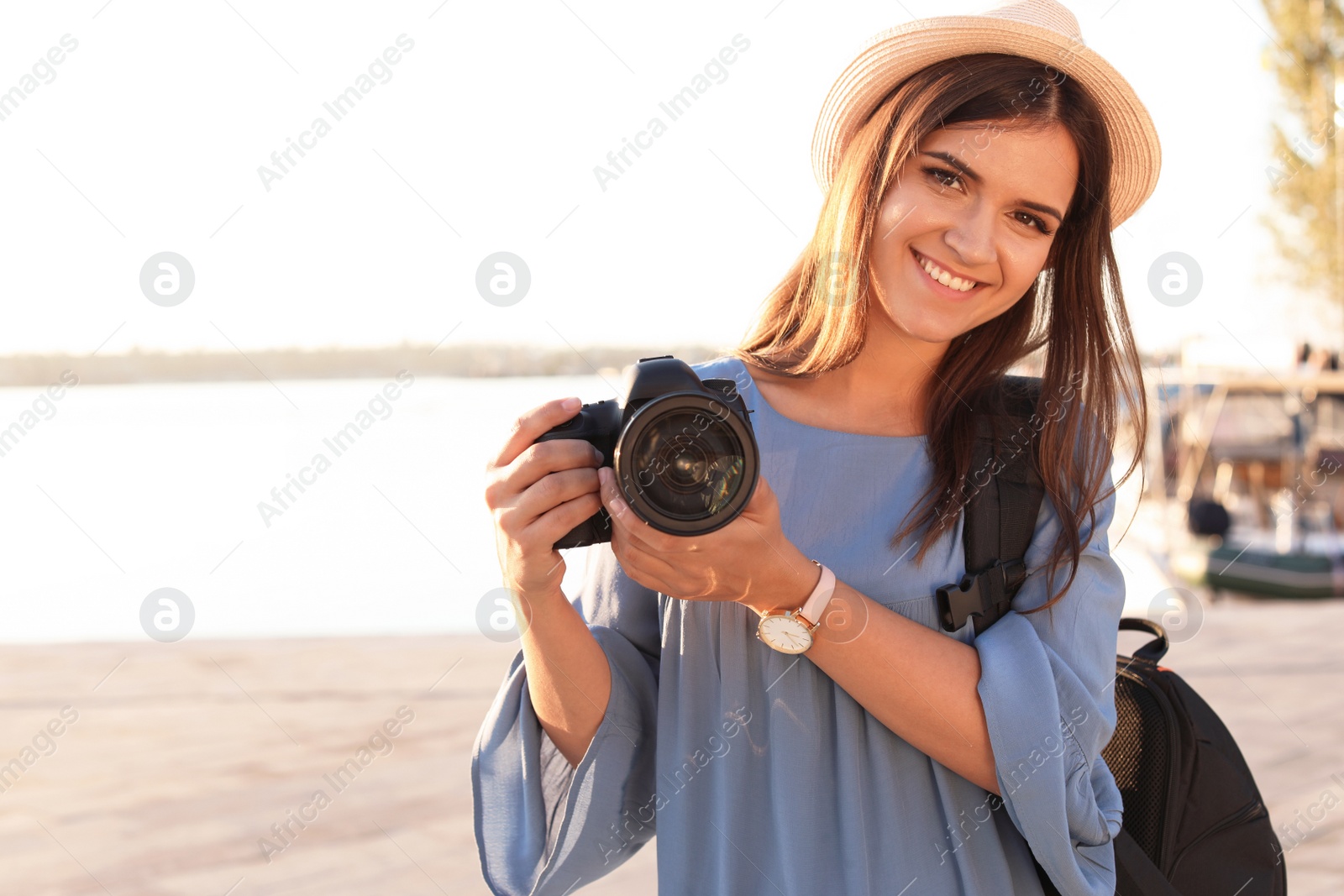 Photo of Young female photographer holding professional camera at pier. Space for text