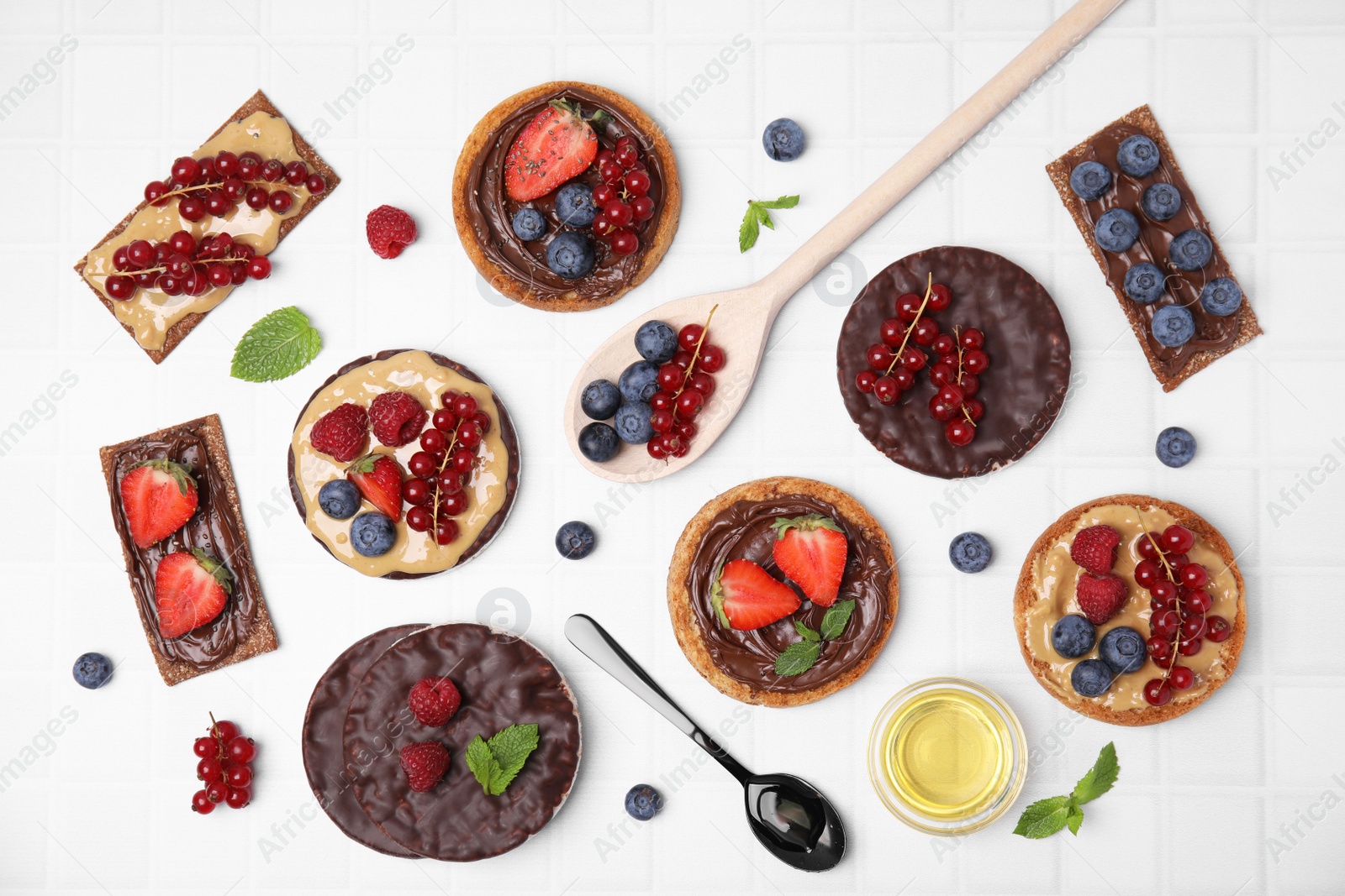 Photo of Fresh rye crispbreads, crunchy rice cakes and rusks with different toppings on white table, flat lay