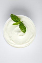 Bowl of fresh sour cream with basil on white background, top view