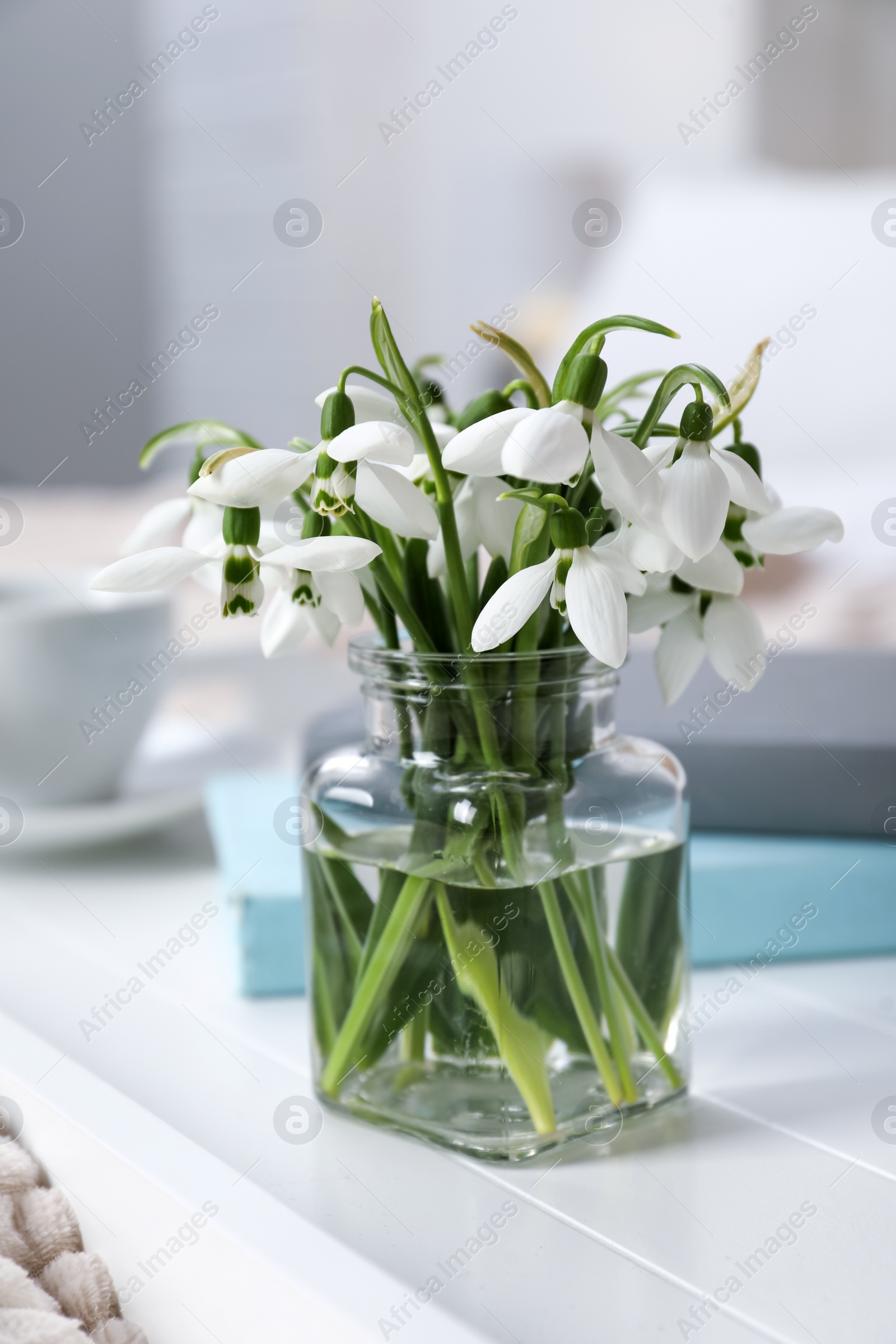 Photo of Beautiful snowdrops, books and cup of coffee on tray in bedroom