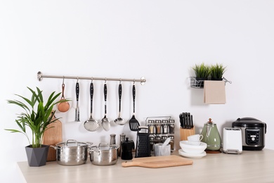 Set of clean cookware, dishes, utensils and appliances on table at white wall