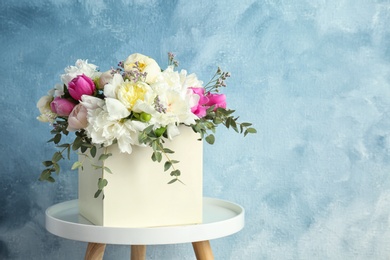 Photo of Box with bouquet of beautiful flowers on table against color background