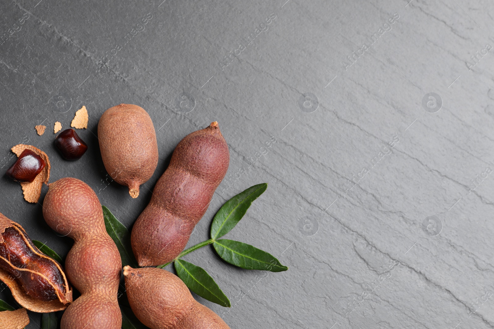 Photo of Delicious ripe tamarinds and leaves on black table, flat lay. Space for text