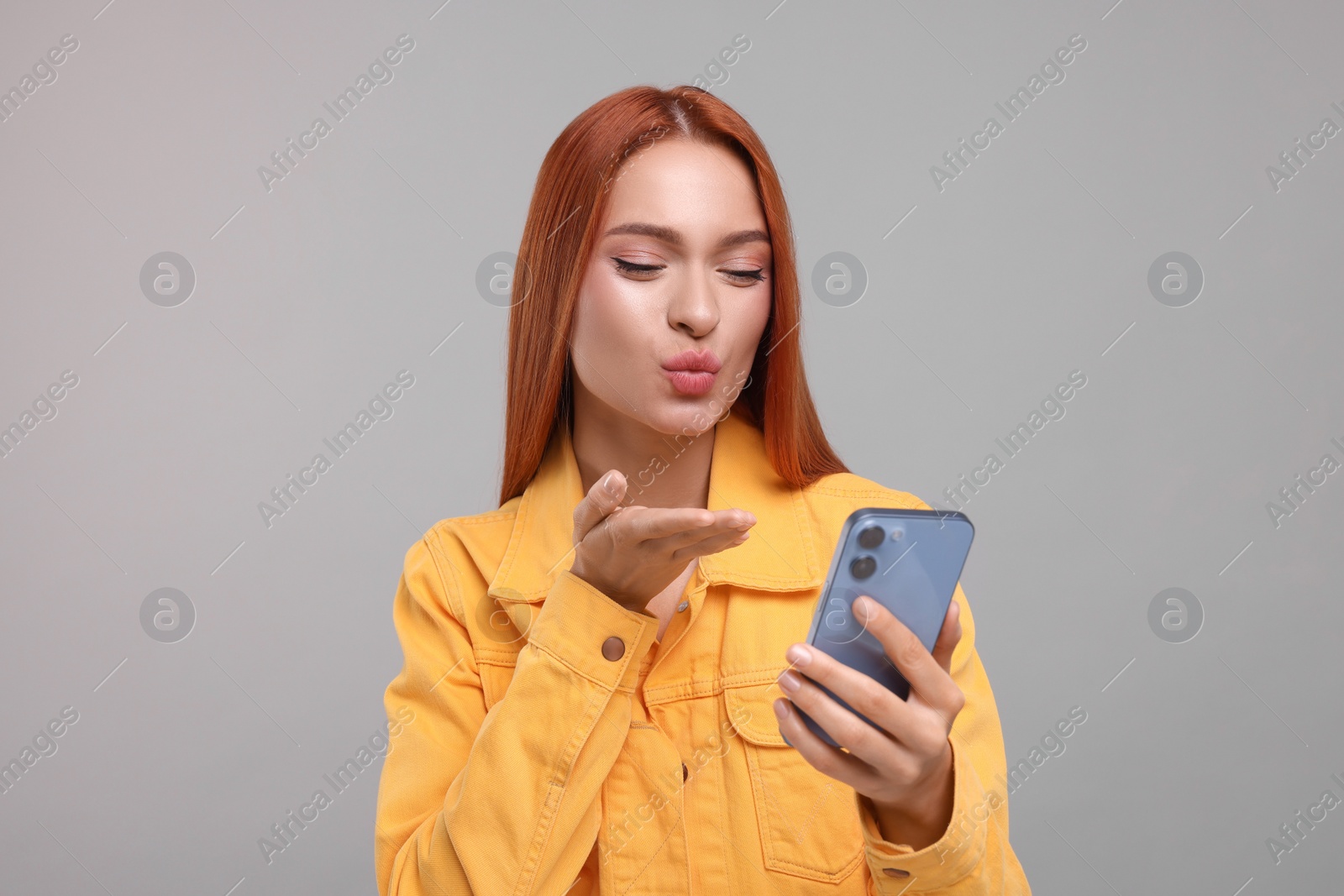 Photo of Beautiful woman blowing kiss during video chat via smartphone on grey background