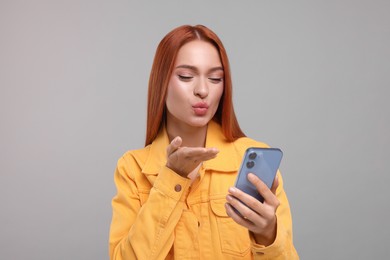 Beautiful woman blowing kiss during video chat via smartphone on grey background