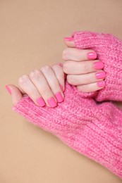 Photo of Woman showing her manicured hands with pink nail polish on dark beige background, top view