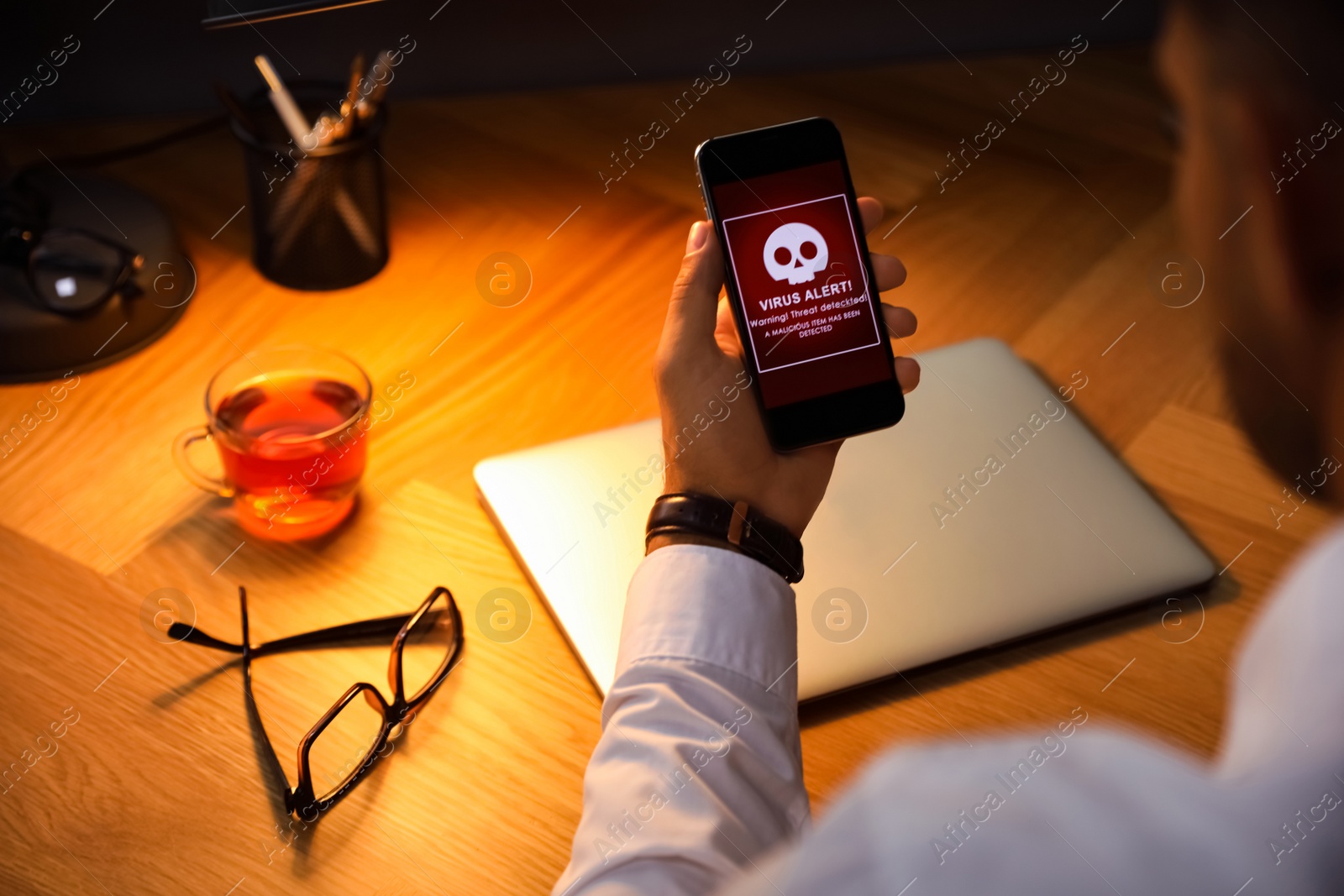 Photo of Man holding smartphone with warning about virus attack at table, closeup