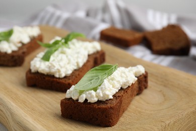 Photo of Bread with cottage cheese and basil on wooden board, closeup