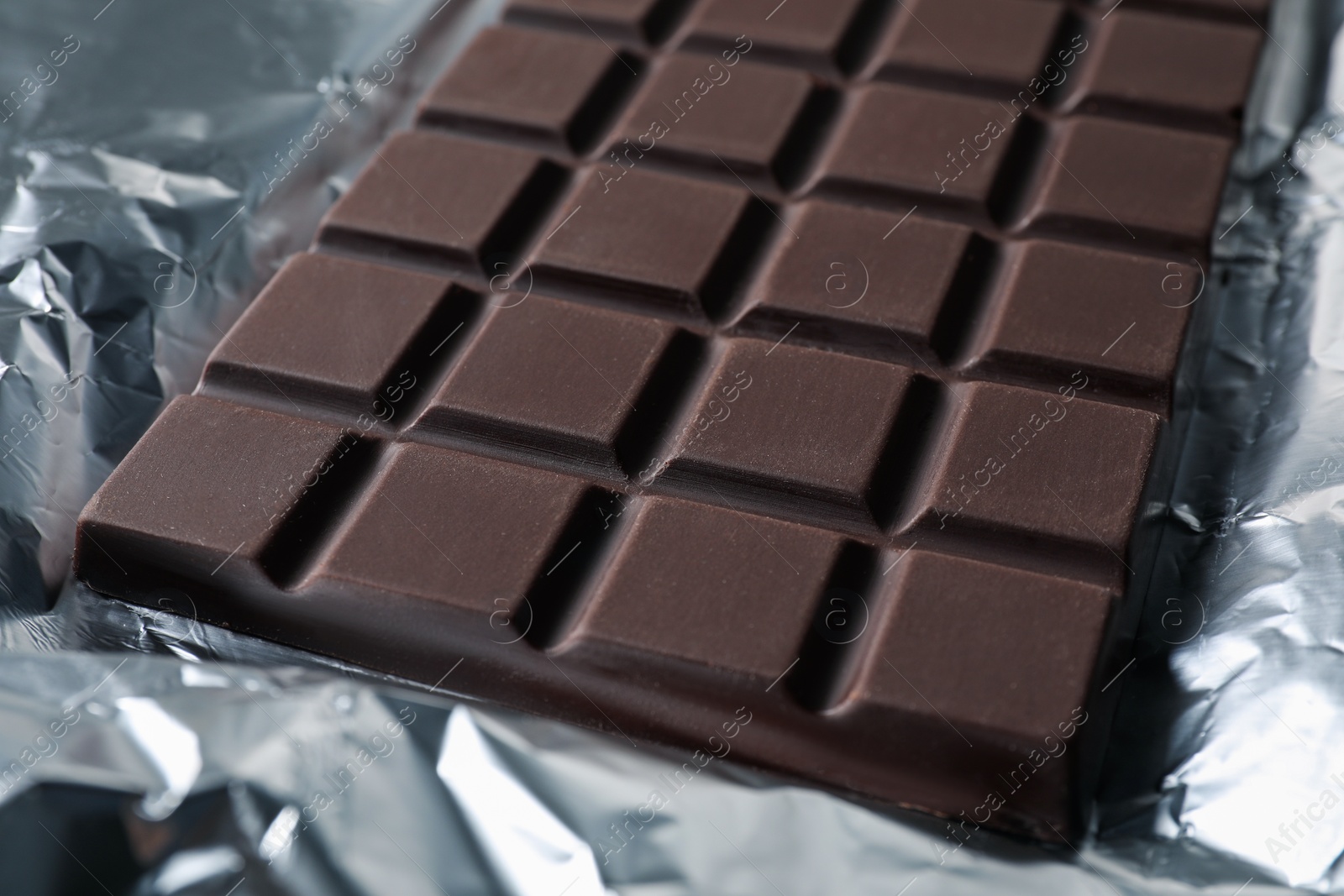 Photo of Delicious dark chocolate bar on foil, closeup