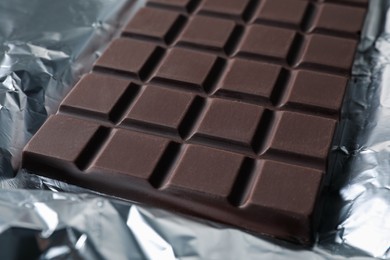 Photo of Delicious dark chocolate bar on foil, closeup