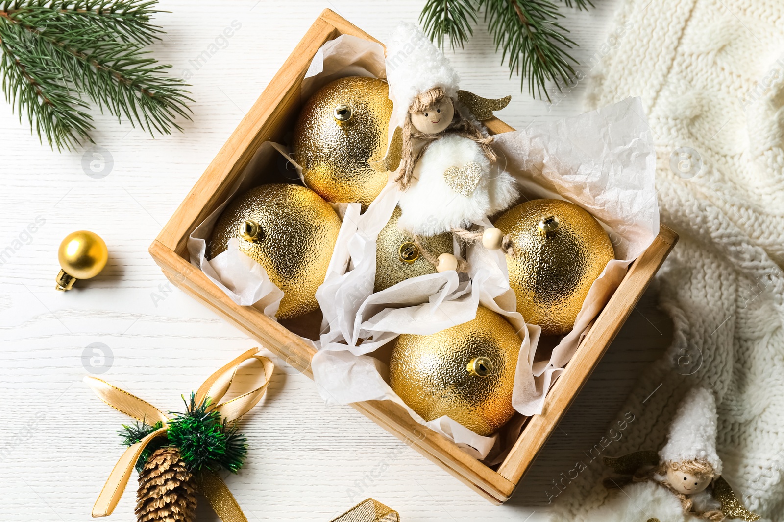 Photo of Beautiful golden Christmas baubles in crate on white wooden table, flat lay