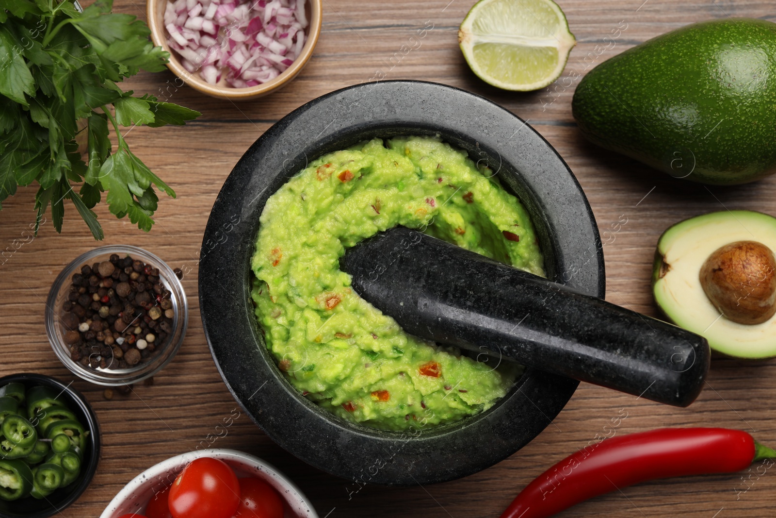 Photo of Delicious guacamole in mortar and ingredients on wooden table, flat lay