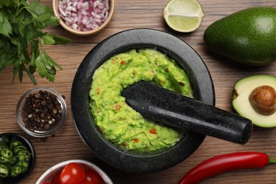 Delicious guacamole in mortar and ingredients on wooden table, flat lay