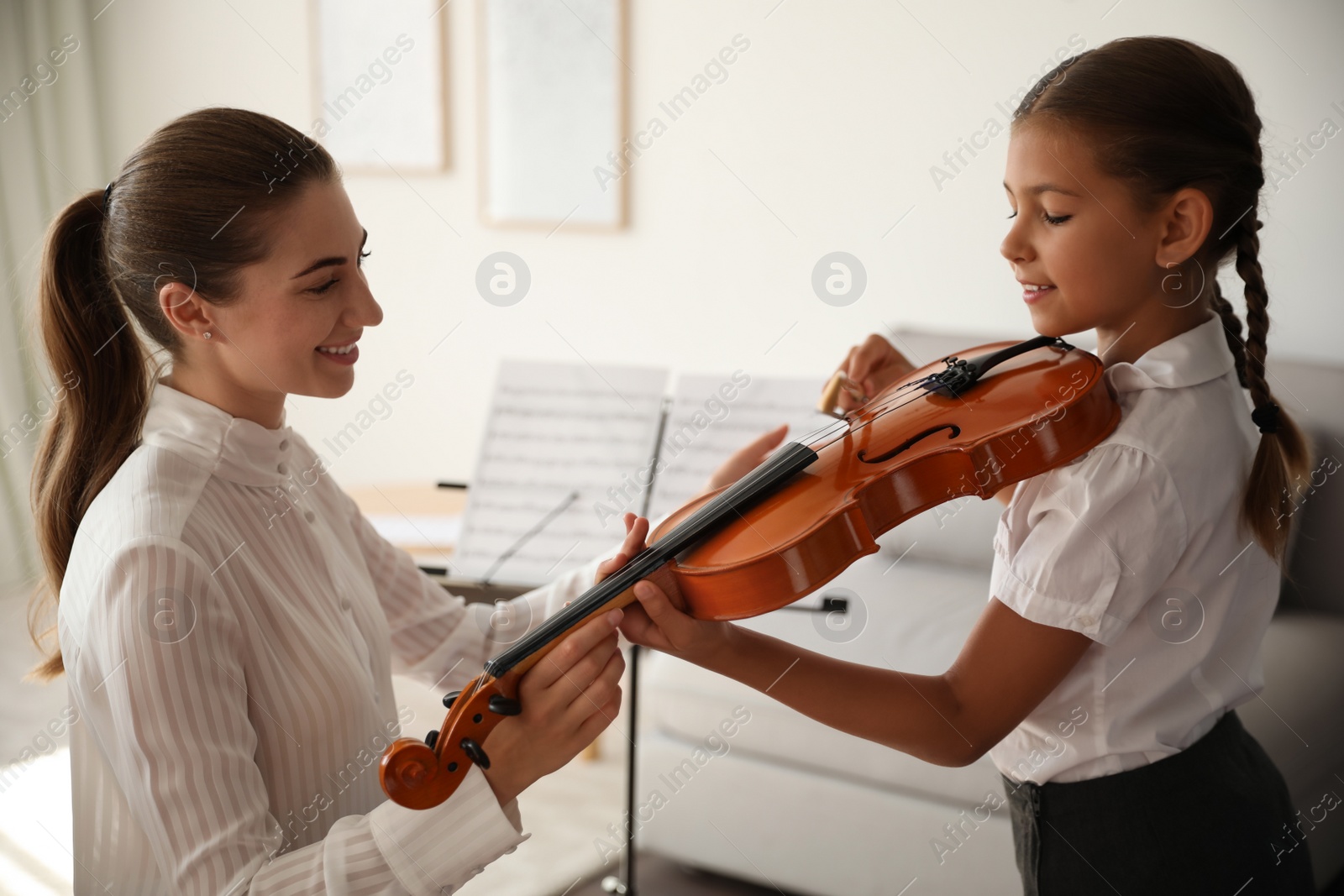 Photo of Young woman teaching little girl to play violin indoors