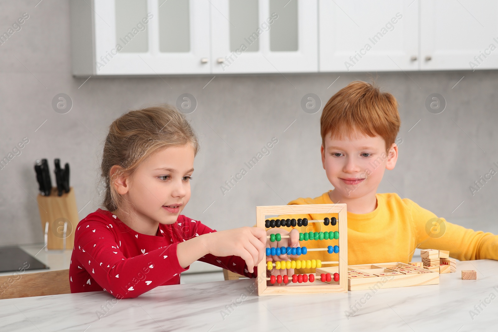 Photo of Happy children playing with abacus at white marble table in kitchen. Learning mathematics with fun