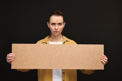 Photo of Angry woman holding blank cardboard banner on black background, space for text