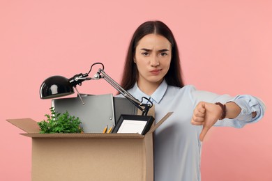 Photo of Unemployment problem. Unhappy woman with box of personal office belongings showing thumbs down on pink background