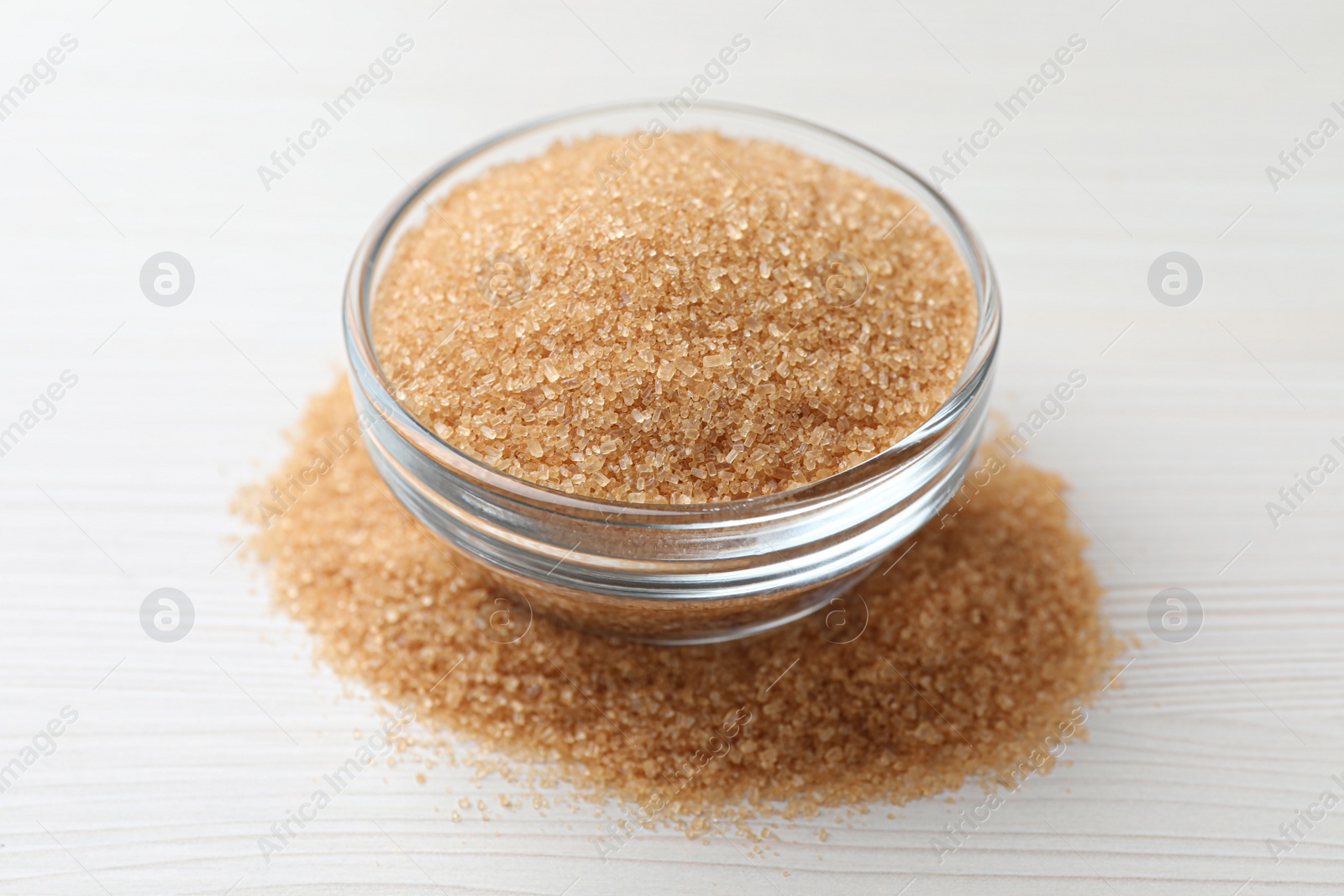 Photo of Brown sugar and glass bowl on white wooden table, closeup