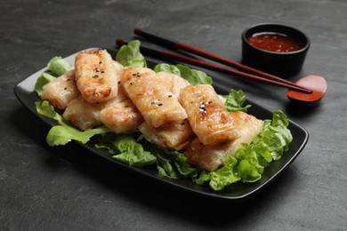 Photo of Tasty fried spring rolls, lettuce and sauce on black table