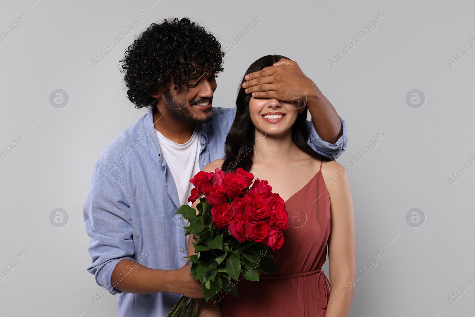 Photo of International dating. Handsome man presenting roses to his beloved woman on light grey background