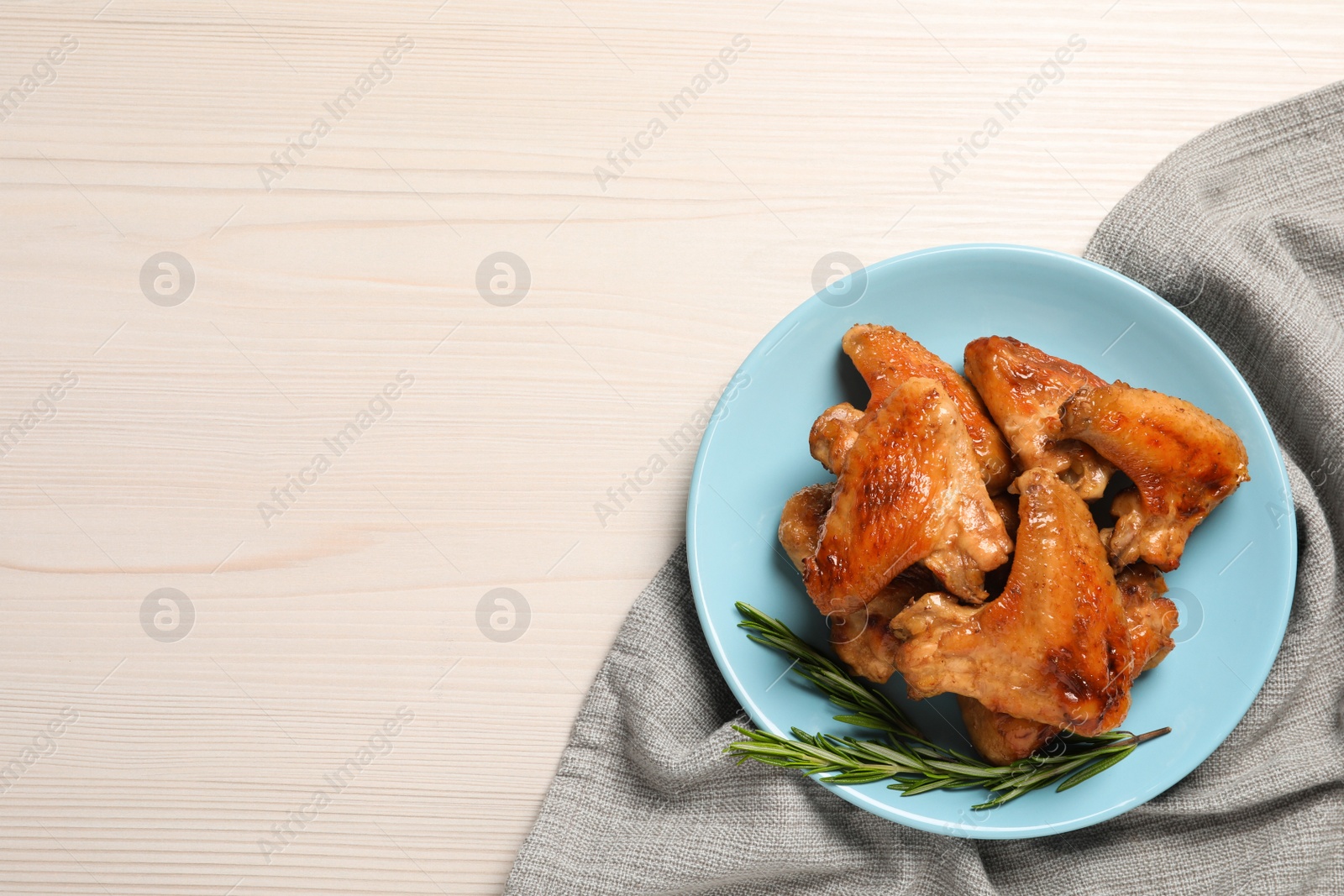 Photo of Plate with delicious fried chicken wings and sprig of rosemary on white wooden table, top view. Space for text