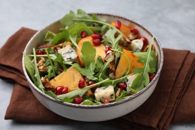 Tasty salad with persimmon, blue cheese, pomegranate and walnuts served on light grey table