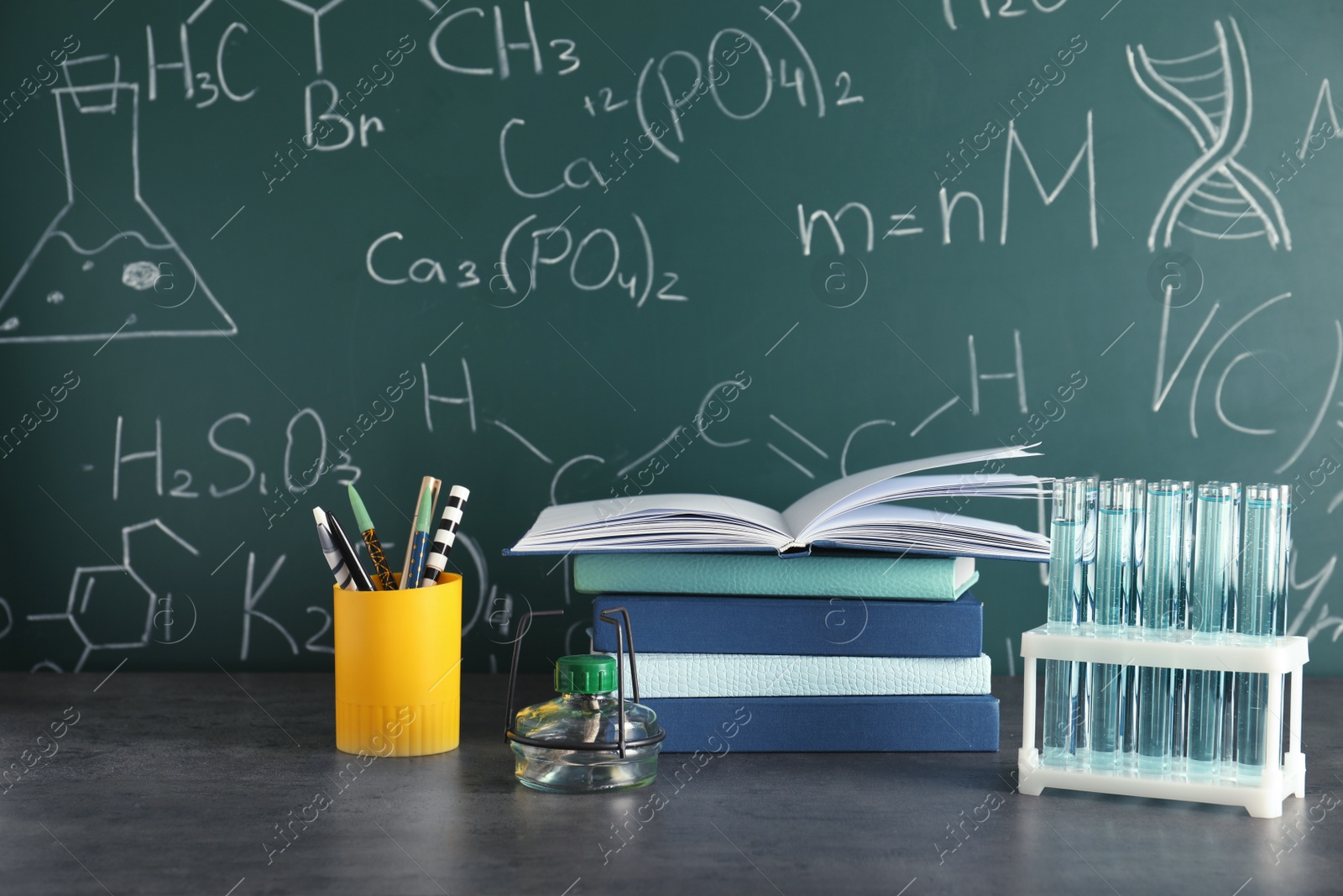 Photo of Laboratory glassware and school supplies on table against blackboard with chemical formulas