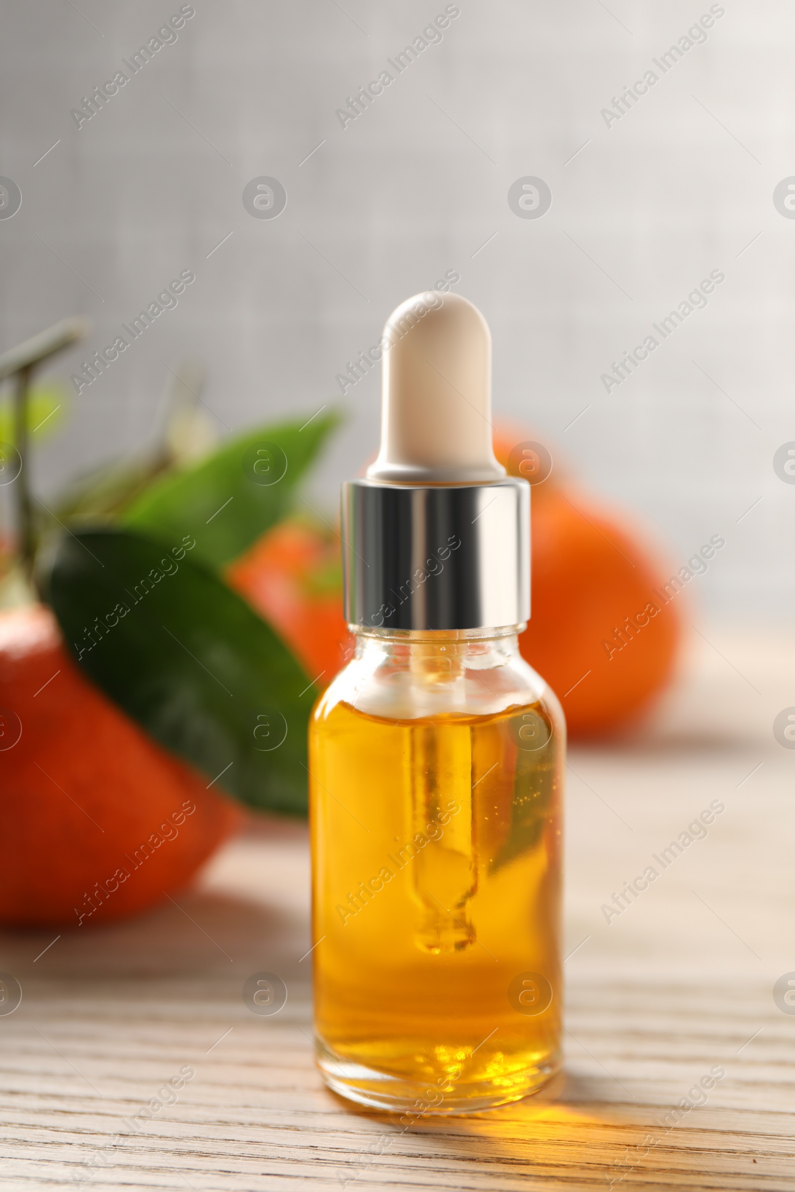 Photo of Bottle of tangerine essential oil and fresh fruits on white wooden table, closeup