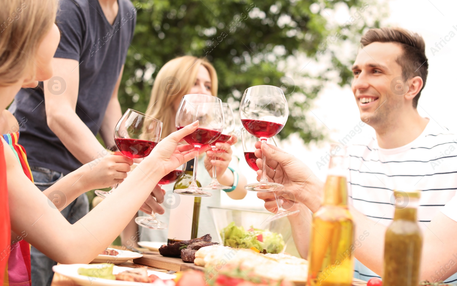 Photo of Young people with glasses of wine at table outdoors. Summer barbecue