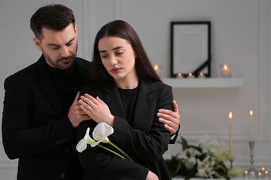 Photo of Sad couple with calla lily flowers mourning indoors, space for text. Funeral ceremony