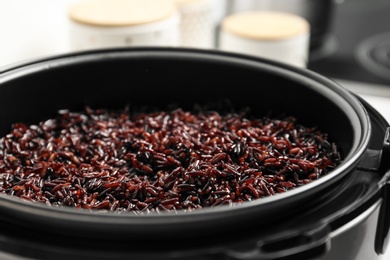 Photo of Modern multi cooker with boiled brown rice in kitchen, closeup