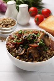 Photo of Delicious lentils with mushrooms, bacon and green onion in bowl served on white table, closeup