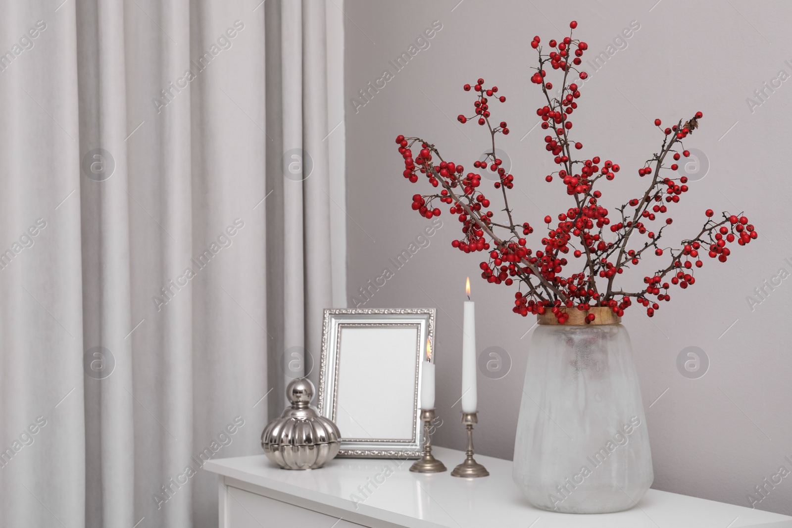 Photo of Hawthorn branches with red berries in vase, candles and frame on table indoors, space for text