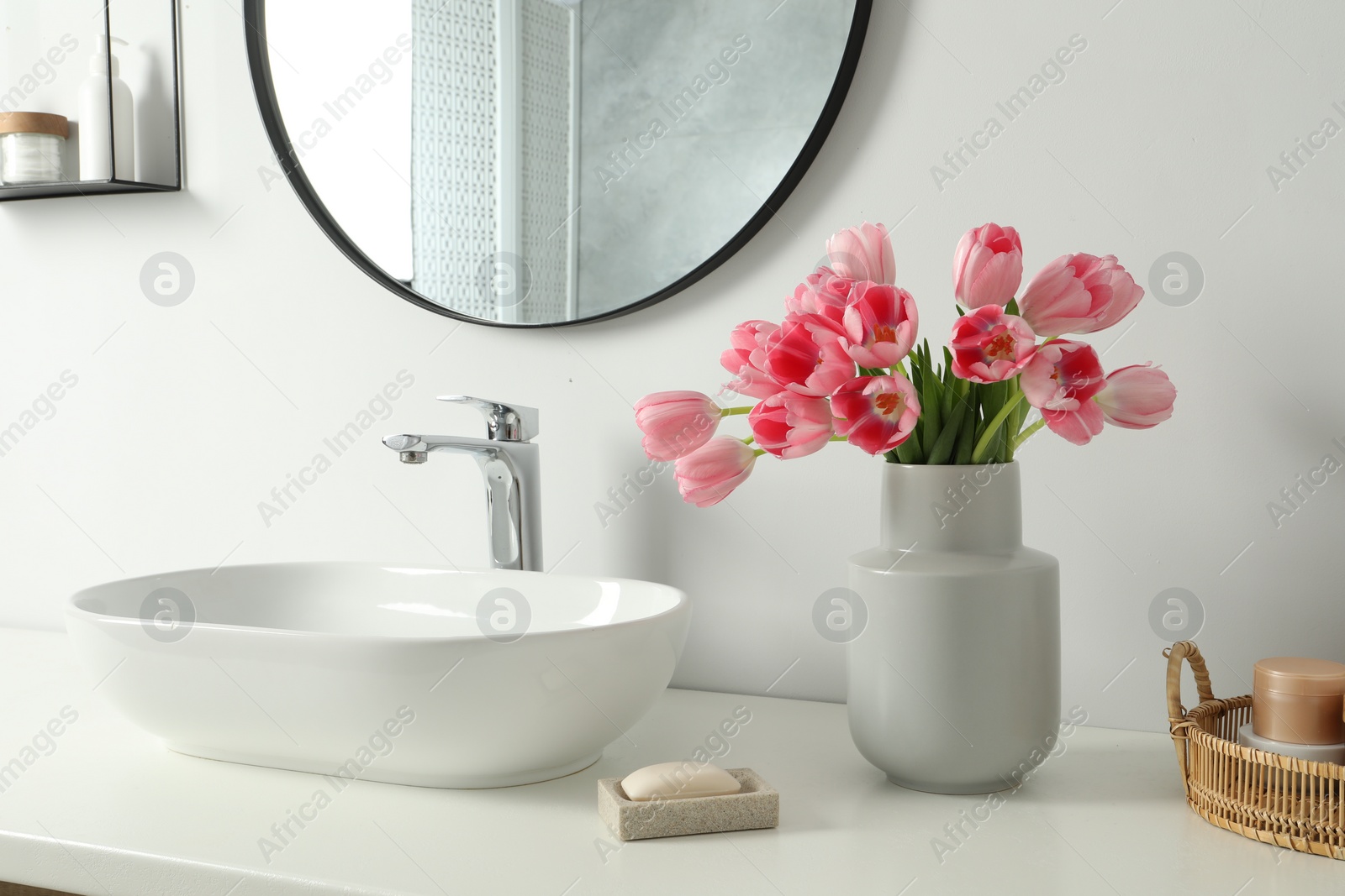 Photo of Vase with beautiful pink tulips and toiletries near sink in bathroom