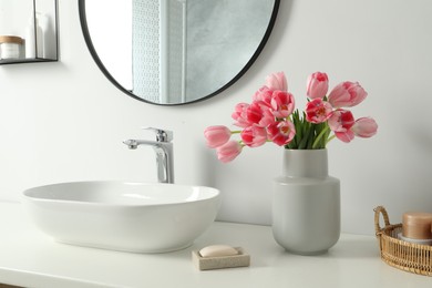 Photo of Vase with beautiful pink tulips and toiletries near sink in bathroom