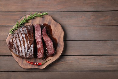 Photo of Delicious grilled beef meat, chili pepper and rosemary on wooden table, top view. Space for text